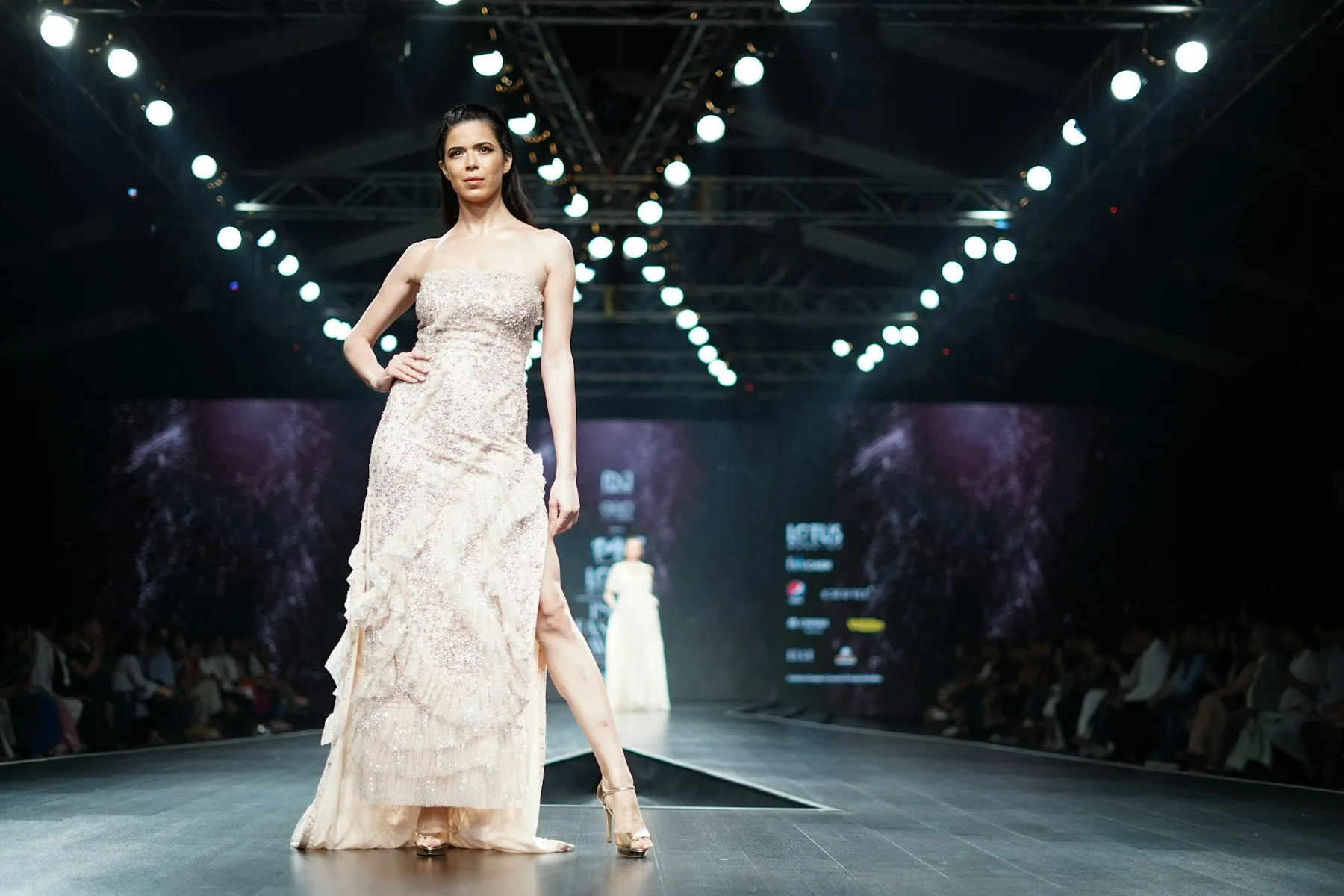 A model in an ivory gown poses at the end of a lit runway