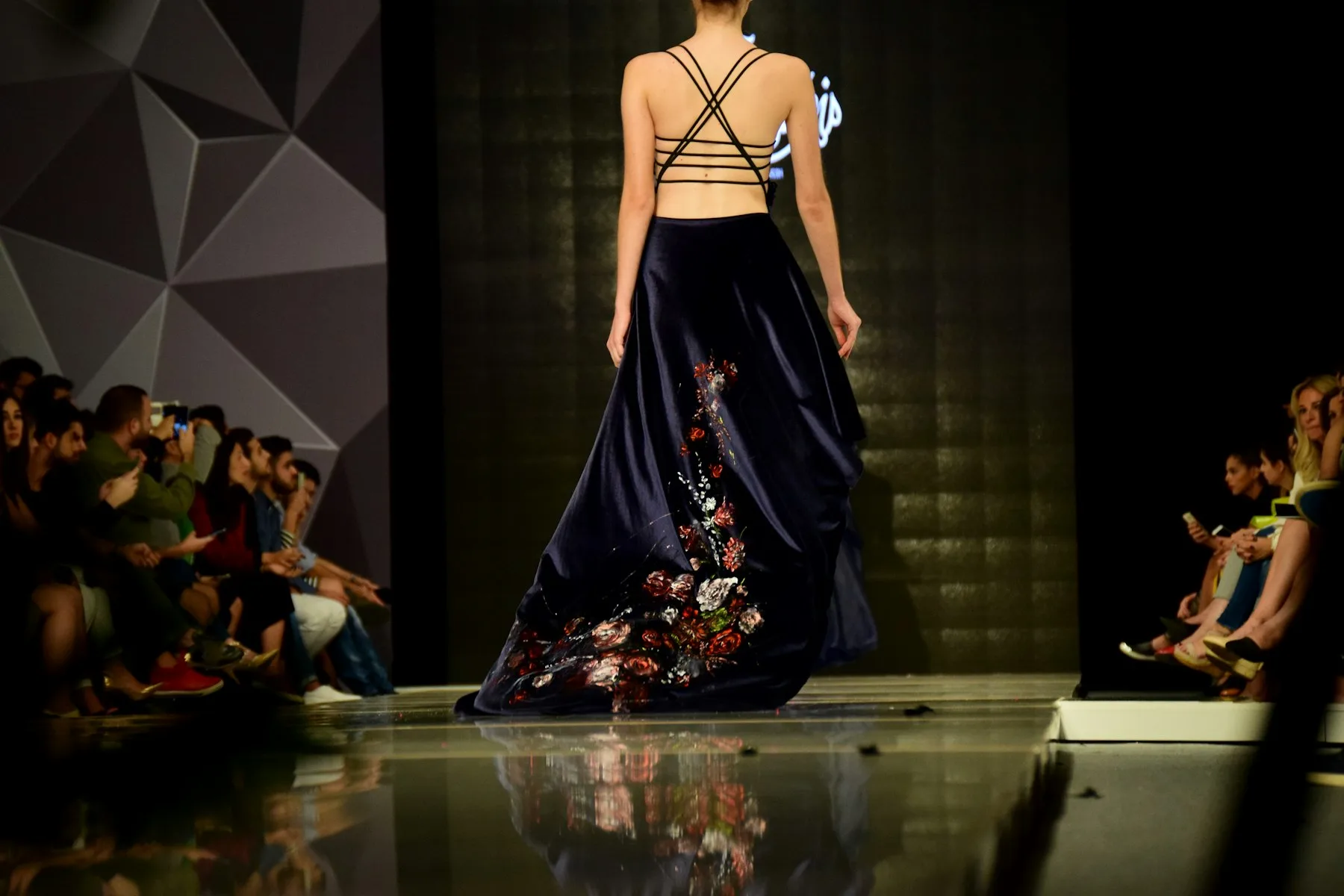 A model in an embroidered gown walks toward a lit stage